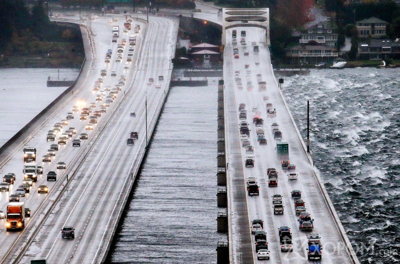 Eastbound traffic lanes, right, on Interstate 90 are dampened by wind-driven waves from the south as the floating bridge calms Lake Washington to the north, left, Tuesday, Nov. 17, 2015, in Seattle. Rain and high winds snarled the morning commute in the Puget Sound area and the Inland Northwest braced for severe weather that could include wind gusts to 70 mph. The National Weather Service says a Pacific storm system arriving Tuesday may include sustained winds of 45 mph that could topple trees and cause power outages. (AP Photo/Elaine Thompson)